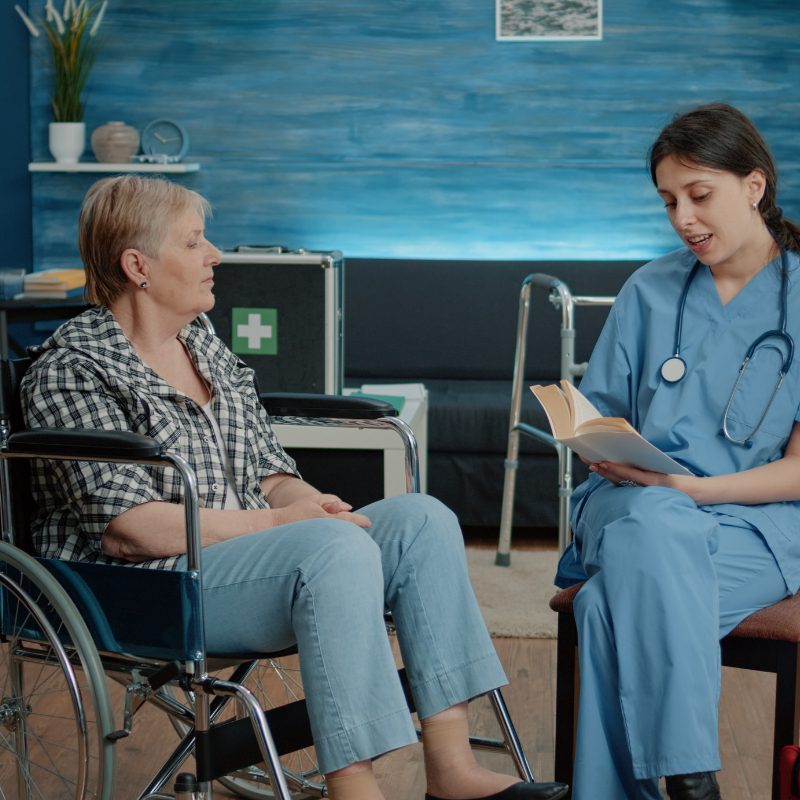 A nurse engages in conversation with an elderly woman seated in a wheelchair, showcasing compassion and care.