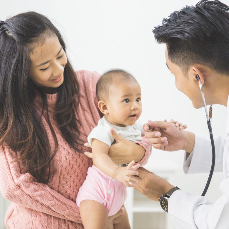 A doctor carefully examines a baby during a routine check-up in a clinical setting.