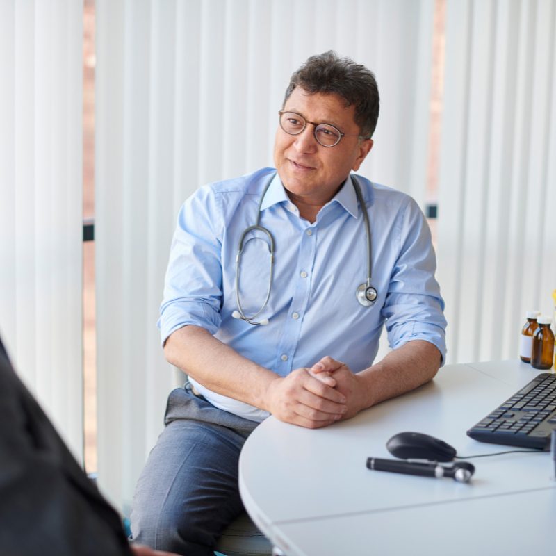 A man converses with a doctor at a table, discussing health matters.